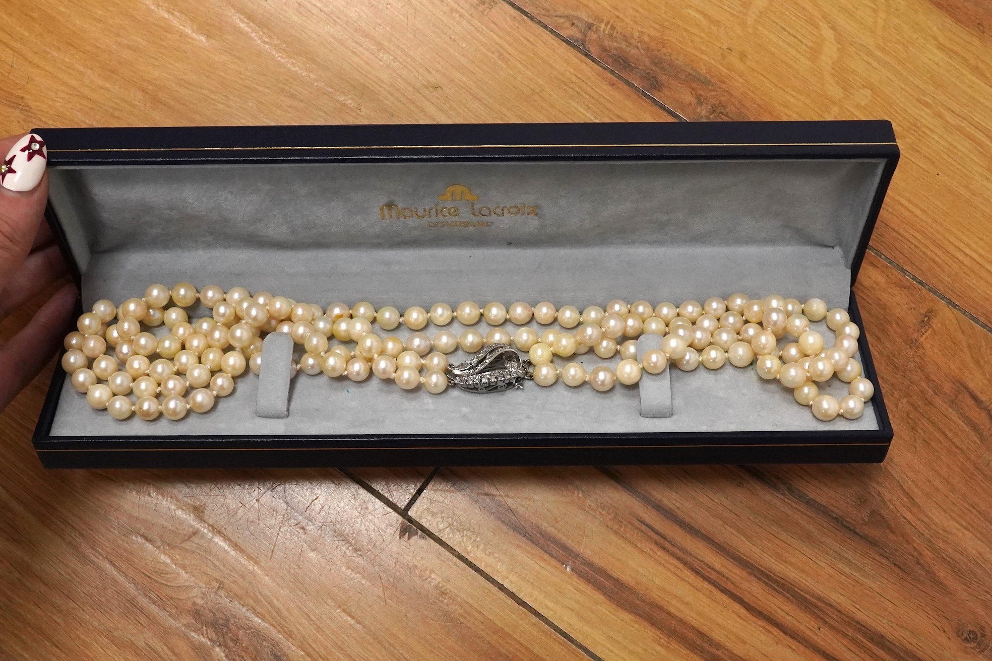 A twin strand cultured pearl necklace with a diamond cluster set white metal scroll shaped clasp, 60cm.